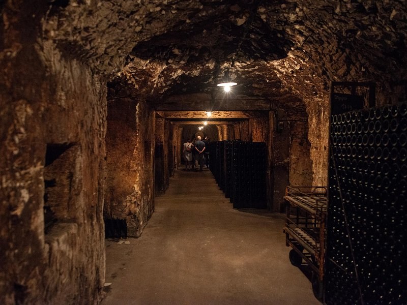 A long chalk gallery lit by a single lamp, bottles stacked along its walls