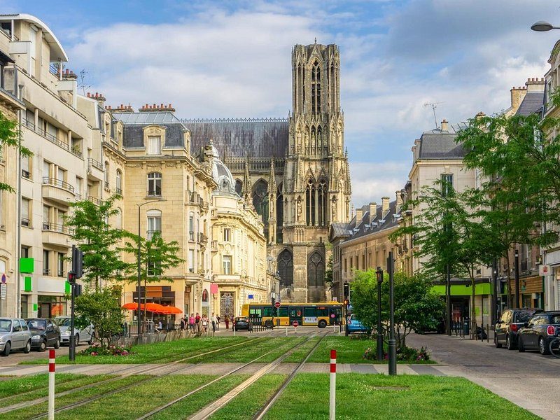 A tree-lined street with tram tracks in the grass and a Gothic tower at its end