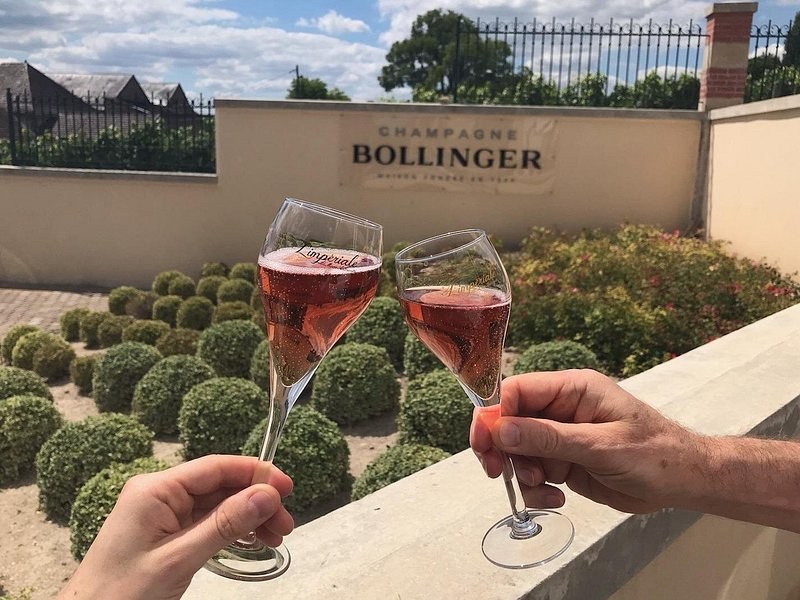 Two glasses of rosé raised before the Bollinger sign and a clipped garden